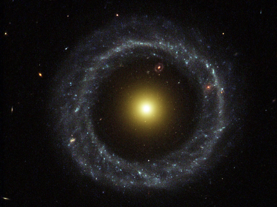 On the outside is a ring dominated by bright blue stars, while near the center lies a ball of much redder stars that are likely much older. Between the two is a gap that appears almost completely dark... Coincidentally, visible in the gap (at about one o'clock) is yet another ring galaxy that likely lies far in the distance.